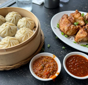 Steamed momos in a bamboo steamer, fried momos and bowls of achar and chilli chutney