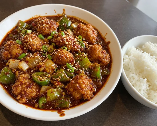 Tangra masala chicken: fried chicken in a thick dark red masala gravy with green pepper, onion and spring onion, with a bowl of rice
